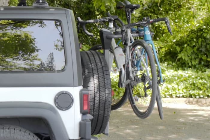 grey jeep wrangler with attached Yakima spare tire bike rack and two bicycles