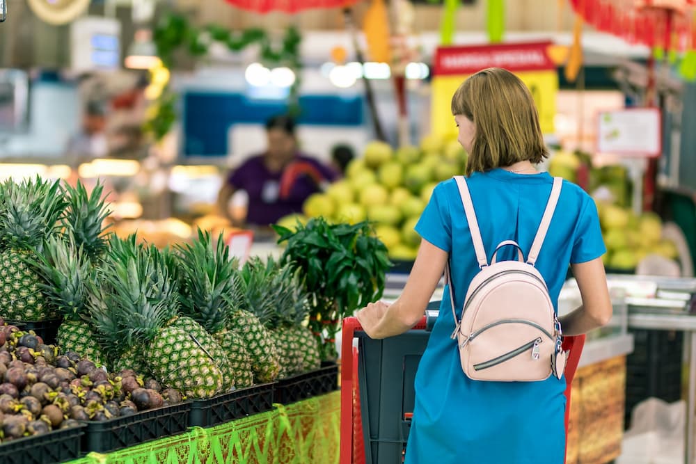 young woman in blue dress with small pink backpack shopping for groceries