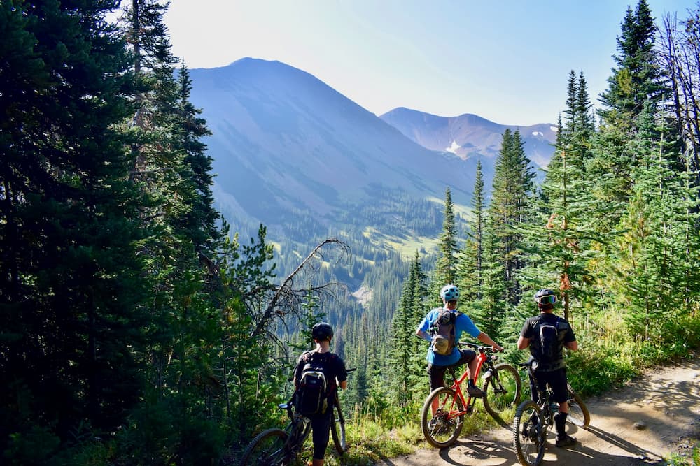 three cyclists with biking backpacks riding on bicycles during daytime in Canadian mountains